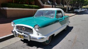 Teal and white vintage convertible car parked on a city street with brick buildings in the background.