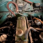 Engine bay of an older vehicle with a green valve cover and brown rubber hoses.