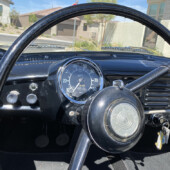 Close-up of a vintage car dashboard with a large circular speedometer, steering wheel, and ignition keys in view.