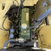 Top-down view of a vintage car engine bay featuring a green inline engine, black air filter housing, radiator, hoses and wiring.